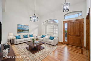 Living room featuring high vaulted ceiling, a chandelier, plenty of natural light, and light wood-type flooring