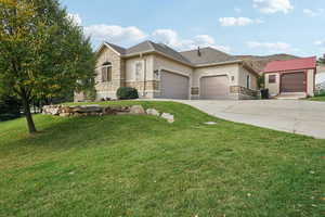 View of front facade with stucco siding, stone siding, a front yard, driveway, and an outbuilding