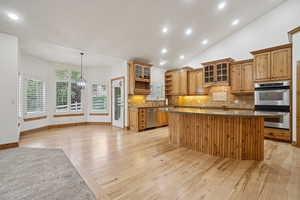 Kitchen with open shelves, tasteful backsplash, glass insert cabinets, light wood finished floors, and recessed lighting