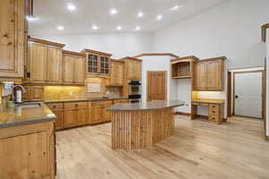 Kitchen with light wood-type flooring, tasteful backsplash, glass insert cabinets, a center island, and high vaulted ceiling