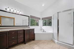 Bathroom with a stall shower, a bath, double vanity, lofted ceiling, and light tile patterned floors
