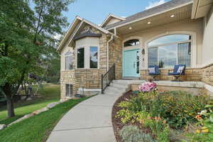 Property entrance featuring stone siding, a lawn, stucco siding, and roof with shingles