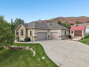 View of front facade featuring stone siding, stucco siding, a front lawn, concrete driveway, and an attached garage