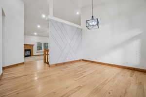 Unfurnished dining area with high vaulted ceiling, light wood-style floors, a glass covered fireplace, recessed lighting, and a chandelier