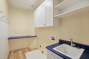 Washroom featuring washer hookup, light wood-style flooring, cabinet space, and electric dryer hookup