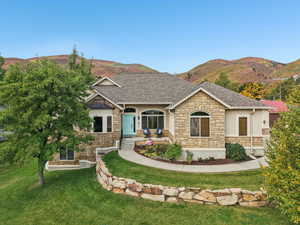View of front of property featuring stone siding, a front lawn, a mountain view, and a shingled roof