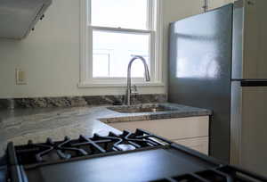 Kitchen view of freestanding refrigerator, ventilation hood, dark stone counters, gas cooktop, and white cabinetry