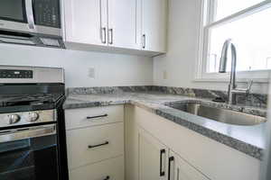Kitchen with white cabinets, stainless steel appliances, and dark stone counters