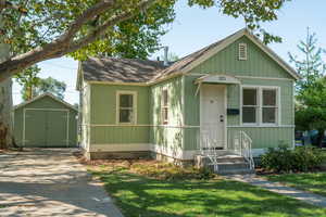 View of front of home featuring a front lawn, roof with shingles, and a shed