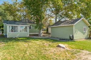 Rear view of property with a yard, an outbuilding, a sunroom, and roof with shingles