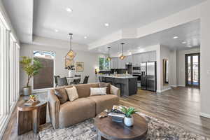 Living area with healthy amount of natural light, a raised ceiling, dark wood finished floors, and recessed lighting