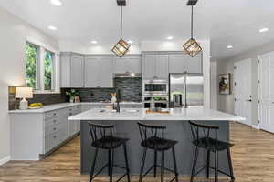 Kitchen featuring backsplash, appliances with stainless steel finishes, gray cabinetry, light stone counters, and recessed lighting