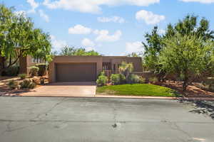 Pueblo revival-style home featuring driveway, stucco siding, an attached garage, and a front lawn