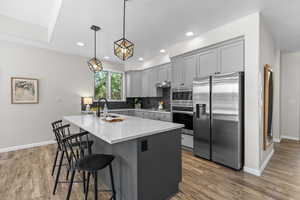 Kitchen with appliances with stainless steel finishes, gray cabinets, decorative light fixtures, backsplash, and light stone counters