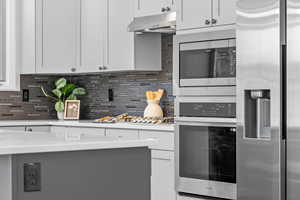 Kitchen featuring appliances with stainless steel finishes, decorative backsplash, white cabinets, exhaust hood, and light stone counters