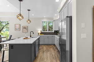 Kitchen featuring gray cabinets, decorative backsplash, stainless steel appliances, pendant lighting, and light wood-style flooring