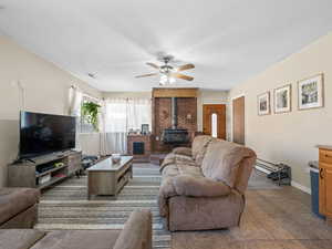 Living area with a wood stove, a ceiling fan, tile patterned flooring, and a textured ceiling
