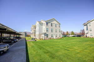 View of property exterior with a yard, stone siding, board and batten siding, a mountain view, and covered parking