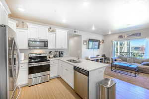 Kitchen featuring appliances with stainless steel finishes, a peninsula, white cabinets, light wood-style flooring, and recessed lighting