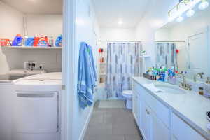 Full bath with light tile patterned flooring, shower / tub combo, vanity, and washer and dryer