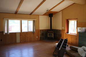 Unfurnished living room with wood walls, a wood stove, wood finished floors, and a wainscoted wall