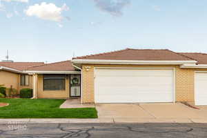 View of front facade with brick siding, driveway, an attached garage, a tile roof, and a front lawn