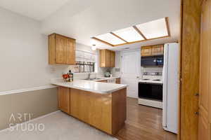 Kitchen with a peninsula, white appliances, light countertops, a textured ceiling, and brown cabinetry