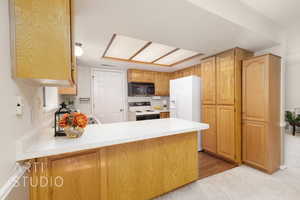 Kitchen featuring light countertops, white appliances, a peninsula, and light carpet