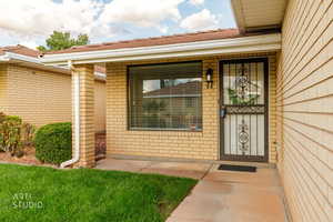 View of exterior entry with brick siding and a yard