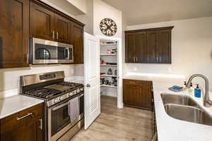 Kitchen with appliances with stainless steel finishes, dark brown cabinetry, laminate floors, and light stone counters