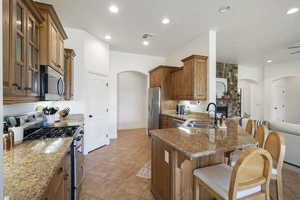Kitchen with arched walkways, appliances with stainless steel finishes, brown cabinets, glass insert cabinets, and recessed lighting