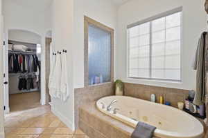 Full bathroom with a jetted tub, a spacious closet, and stone tile floors