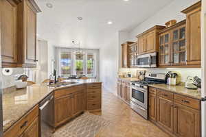 Kitchen featuring brown cabinets, stainless steel appliances, light stone counters, recessed lighting, and a peninsula