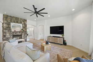 Living room with carpet floors, a stone fireplace, arched walkways, recessed lighting, and a ceiling fan