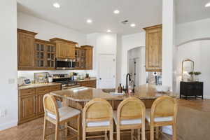 Kitchen with brown cabinets, glass insert cabinets, light stone countertops, a breakfast bar, and recessed lighting