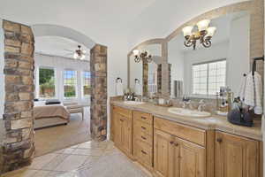 Ensuite bathroom with double vanity, a ceiling fan, decorative columns, and a chandelier