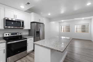 Kitchen featuring appliances with stainless steel finishes, light wood finished floors, a center island, white cabinets, and light stone countertops