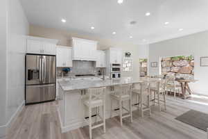Kitchen with appliances with stainless steel finishes, light stone counters, white cabinetry, a large island, and recessed lighting