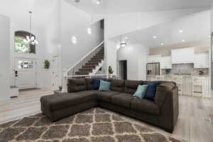 Living area with light wood-type flooring, high vaulted ceiling, stairway, a chandelier, and recessed lighting