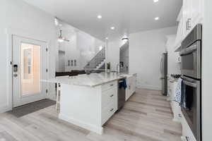 Kitchen featuring white cabinets, stainless steel appliances, light stone counters, open floor plan, and recessed lighting