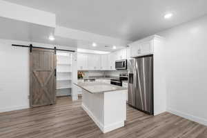 Kitchen with a barn door, stainless steel appliances, white cabinetry, light stone counters, and a kitchen island