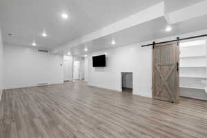 Finished basement with a barn door, light wood-type flooring, and recessed lighting