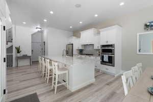 Kitchen with a spacious island, a breakfast bar, white cabinets, light stone countertops, and recessed lighting