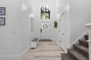 Entryway featuring a towering ceiling, light wood-style flooring, a chandelier, and stairs