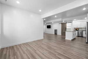 Unfurnished living room featuring a barn door, recessed lighting, and light wood-style flooring