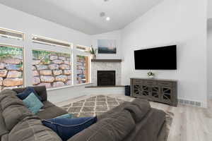 Living room with light wood-style flooring, a stone fireplace, recessed lighting, and high vaulted ceiling