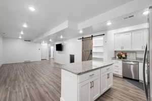 Kitchen with open floor plan, a barn door, light wood-style floors, white cabinetry, and recessed lighting