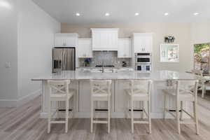 Kitchen featuring white cabinets, a large island, light stone counters, backsplash, and recessed lighting