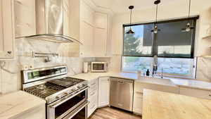 Kitchen featuring stainless steel appliances, exhaust hood, hanging light fixtures, light stone counters, and decorative backsplash