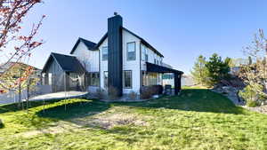 Rear view of house featuring a trampoline, a lawn, a chimney, and board and batten siding
